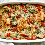 Spinach Artichoke Chicken Bake with golden chicken breasts, melted cheese, spinach, and artichokes in a creamy casserole dish