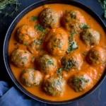 Greek Meatballs with Roasted Red Pepper Sauce served in a skillet with creamy red pepper sauce and fresh herbs.