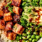 Honey Sriracha Salmon Bowls with glazed salmon bites, white rice, avocado, edamame, sesame seeds, and green onions.