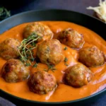 Greek Meatballs with Roasted Red Pepper Sauce topped with fresh thyme in a skillet of smooth roasted pepper sauce.