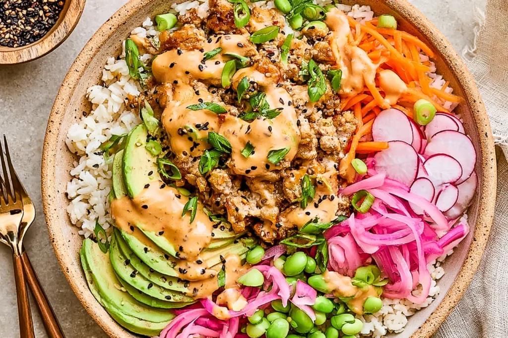 Ground Turkey Rice Bowls with creamy bang bang sauce, avocado slices, pickled onions, edamame, and fresh vegetables over rice