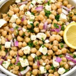 Close-up of Lemony Chickpea Feta Salad with chickpeas, crumbled feta, red onion, parsley, and fresh lemon in a serving bowl