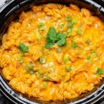 Slow Cooker Chicken Enchilada Pasta with shredded chicken, rotini, melted cheddar cheese, green onions, and cilantro.