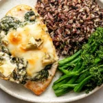 Creamy Spinach Artichoke Chicken Bake served with wild rice and broccolini, topped with melted cheese, spinach, and artichoke hearts.