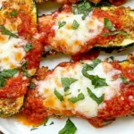 Three Cheese Zucchini Parmesan topped with marinara sauce, melted cheese, and fresh herbs on a white serving plate.
