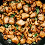 Cashew Chicken with tender glazed chicken pieces, crunchy cashews, green onions, and savory sauce in a skillet