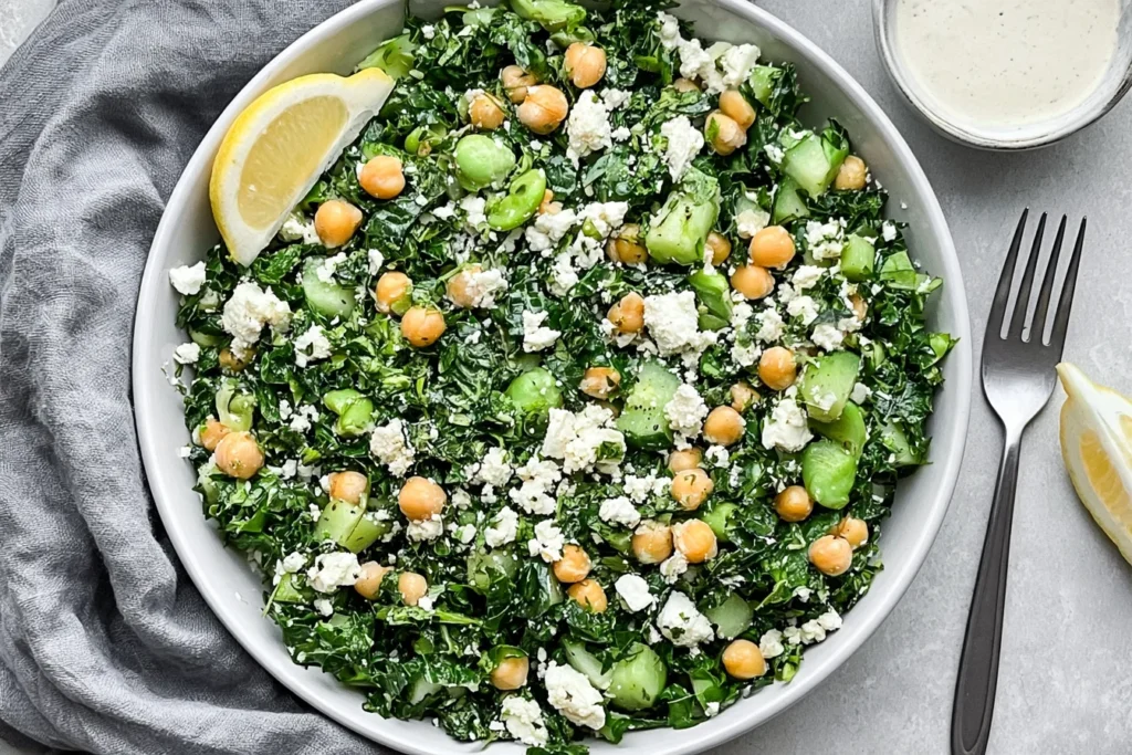 Kale Chickpea Salad with Lemon Tahini Dressing with feta, cucumber, fresh herbs, chickpeas, and lemon in a white bowl.