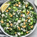 Kale Chickpea Salad with Lemon Tahini Dressing with feta, cucumber, fresh herbs, chickpeas, and lemon in a white bowl.