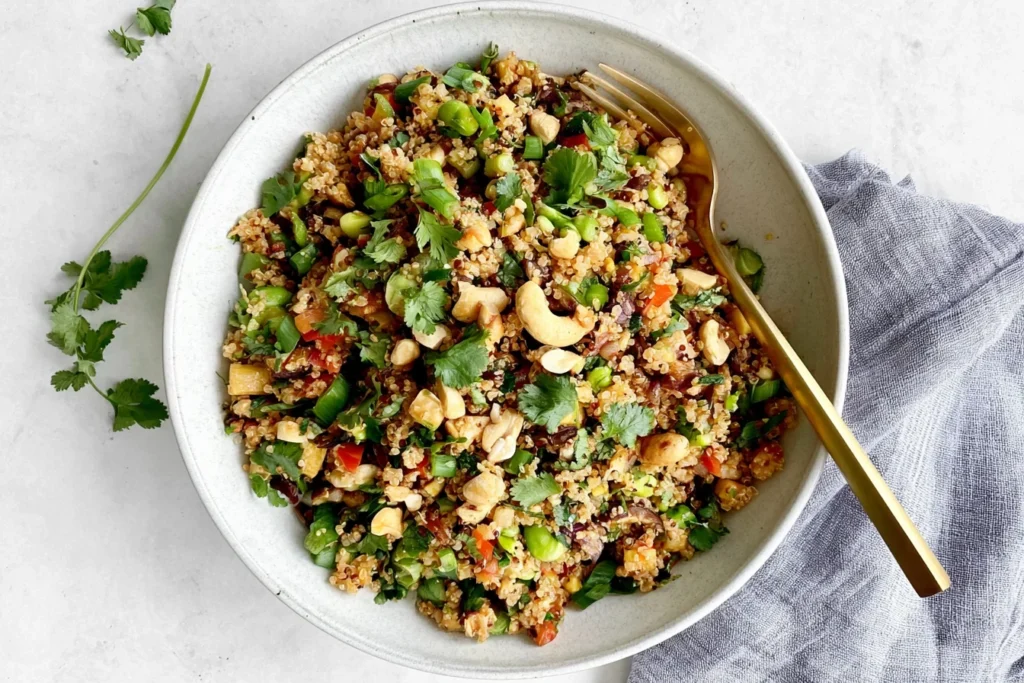 Vegan Thai Quinoa Salad with edamame, fresh cilantro, green onions, red peppers, and crunchy nuts in a flavorful dressing.