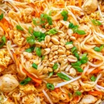Chicken Pad Thai with rice noodles, tender chicken, bean sprouts, carrots, scrambled egg, peanuts, and green onions.