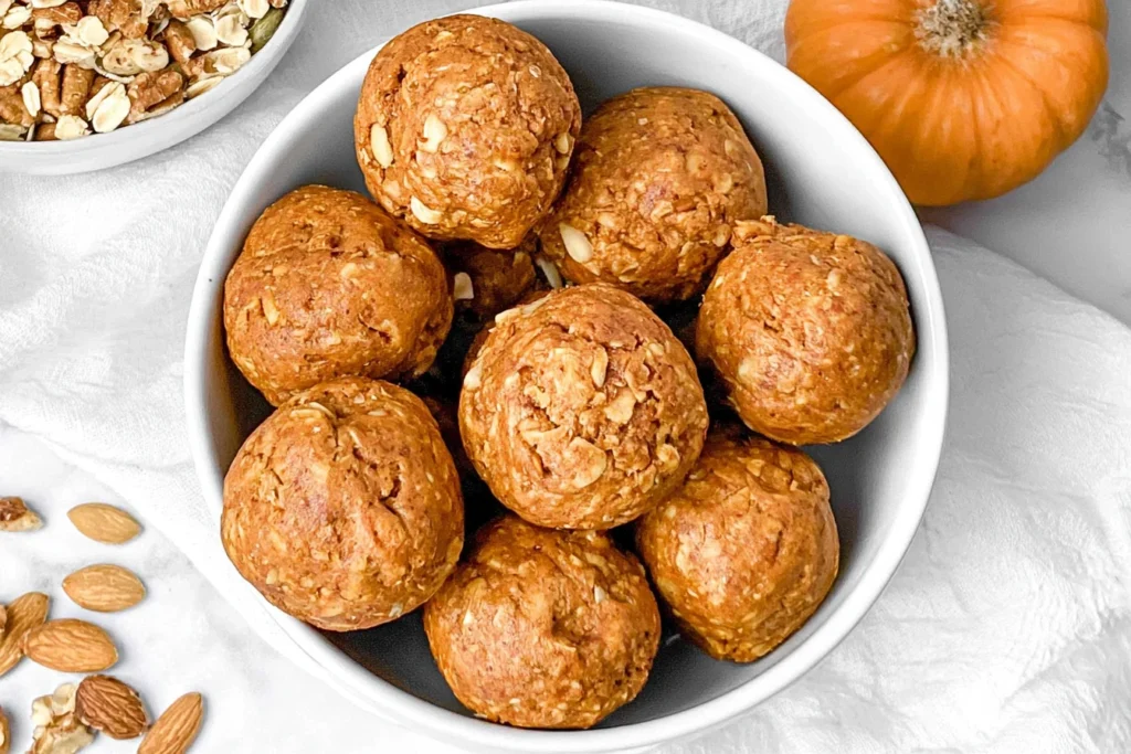 Pumpkin Protein Balls served in a white bowl with rolled oats, almonds, and a fresh pumpkin arranged around the bowl.