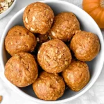 Pumpkin Protein Balls served in a white bowl with rolled oats, almonds, and a fresh pumpkin arranged around the bowl.