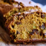 Pumpkin Zucchini Bread sliced on a wooden board, showing a moist golden crumb with shredded zucchini and warm fall spices.