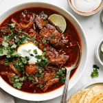 Mexican birria with tender shredded beef in rich red chile consommé, topped with cilantro and lime.