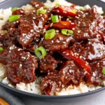 Slow Cooker Mongolian Beef with tender glazed beef, white rice, green onions, red peppers, and sesame seeds.