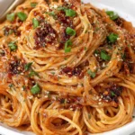 Caramelized Onion Pasta with Chili Oil topped with chili crisp, Parmesan, caramelized onions, and fresh green onions in a white bowl.
