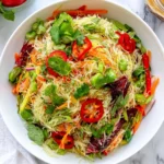Spring Roll Salad with Spicy Ginger Dressing featuring rice noodles, shredded carrots, red bell peppers, fresh cilantro, mint, and colorful vegetables in a white bowl.