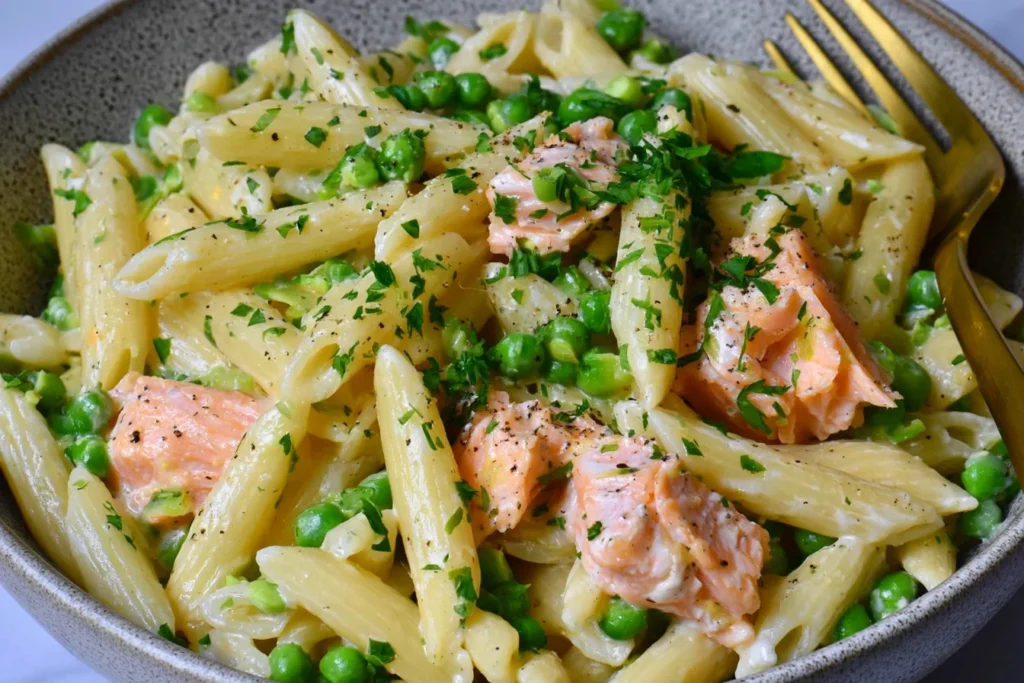 Salmon and Pea Pasta with Lemon featuring tender salmon chunks, penne pasta, sweet green peas, and creamy crème fraîche sauce topped with fresh parsley.