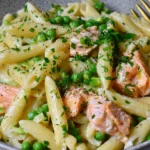 Salmon and Pea Pasta with Lemon featuring tender salmon chunks, penne pasta, sweet green peas, and creamy crème fraîche sauce topped with fresh parsley.